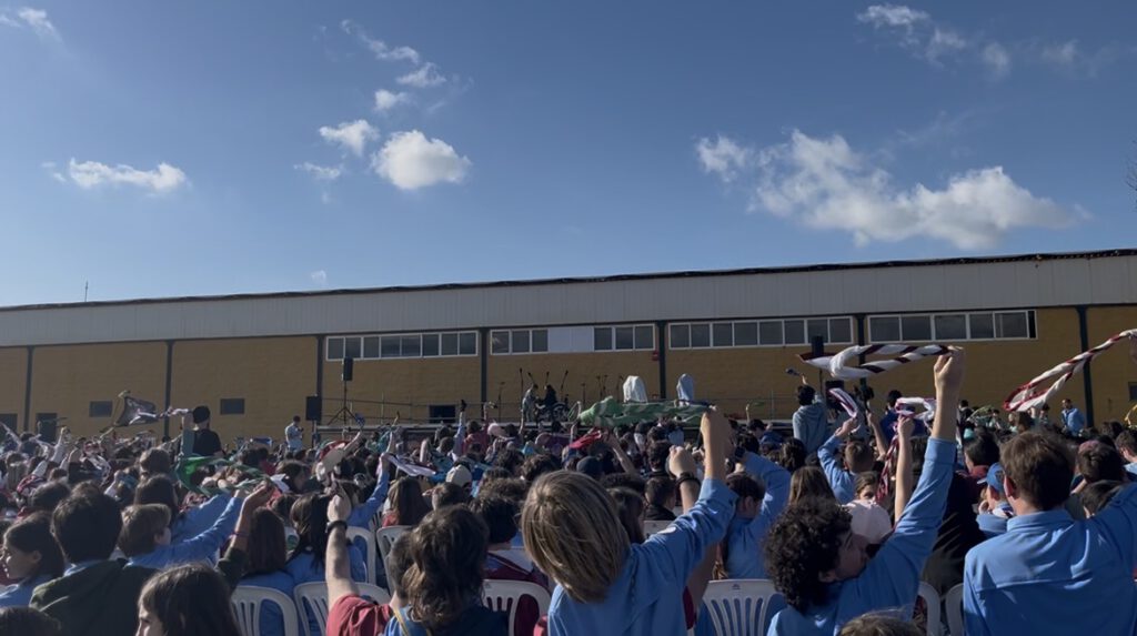 Festival de la canción de Cádiz 2026, scouts al aire libre con numerosos participantes reunidos frente a un escenario, levantando sus pañuelos.