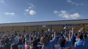 Festival de la canción de Cádiz 2026, scouts al aire libre con numerosos participantes reunidos frente a un escenario, levantando sus pañuelos.