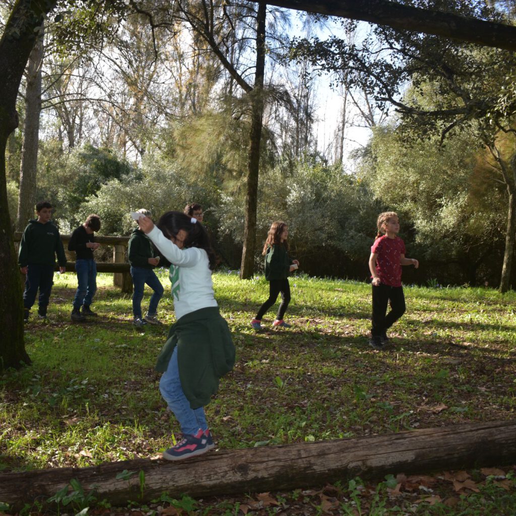 Grupo de niños scouts realizando actividades y juegos al aire libre en un bosque, caminando y jugando entre árboles en un entorno natural.